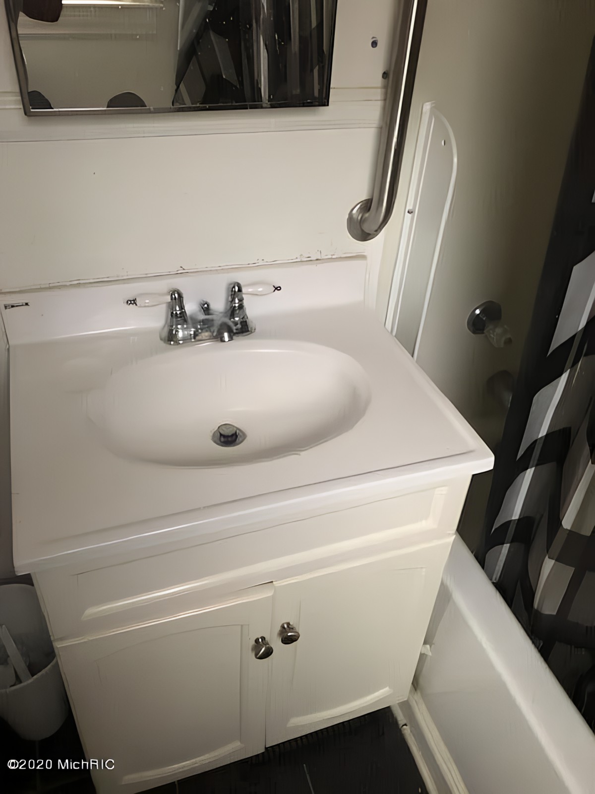 A bathroom sink with a white cabinet and chrome faucet, accompanied by a handrail.