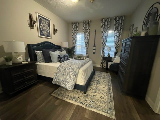 A cozy and elegantly decorated bedroom with a neatly made bed, patterned rug, and stylish curtains.