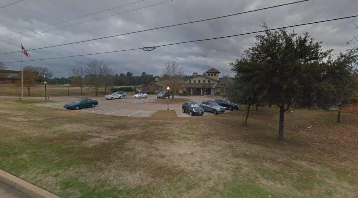 A parking lot with several cars in front of a building under a cloudy sky.