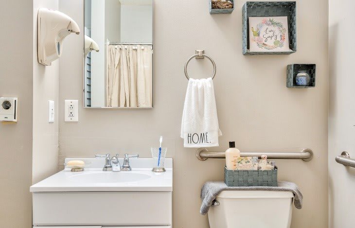 A well-organized bathroom with a mirror, sink, towel, and decorative items on shelves.
