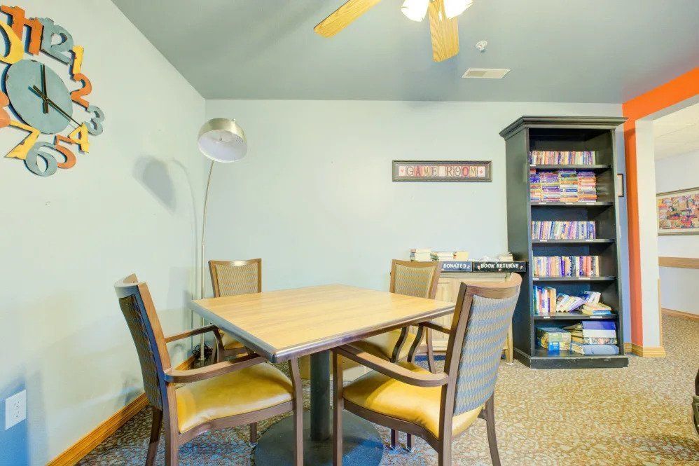 A cozy study room with a table and chairs, featuring a bookshelf and a standing lamp.