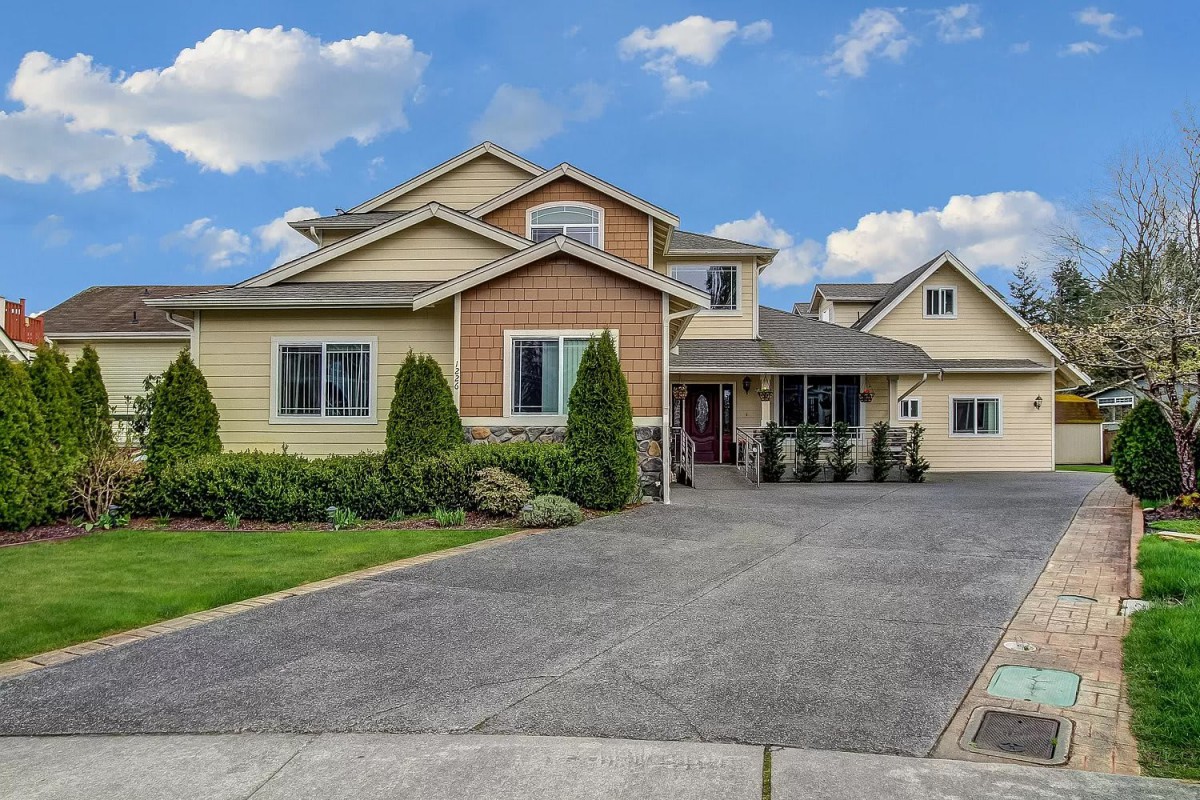 A modern suburban house with a spacious driveway and neatly trimmed landscaping under a partly cloudy sky.