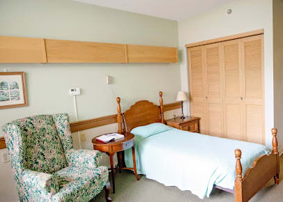 A simple bedroom with a single bed, an armchair, and wooden furniture.