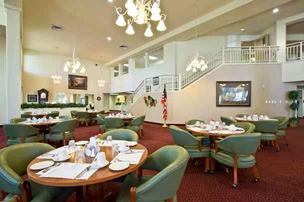 An elegant restaurant interior with neatly set tables and comfortable chairs, illuminated by chandeliers.