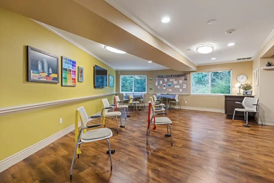 A well-lit meeting room with yellow walls, wooden floors, and chairs arranged in a circle.