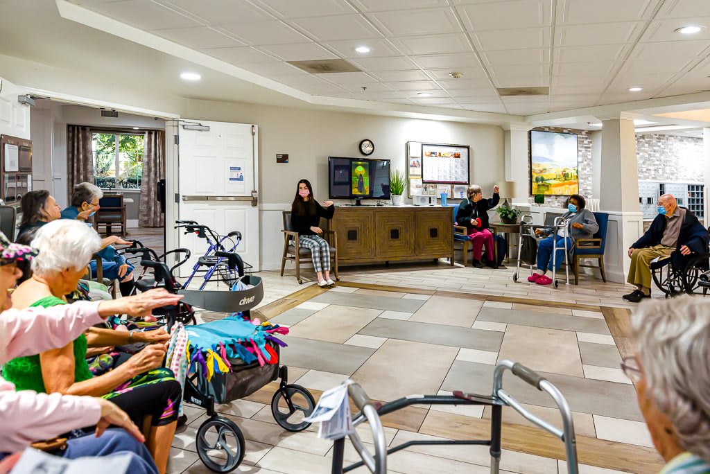 A communal area in a senior living facility with several residents seated and mobility aids nearby.