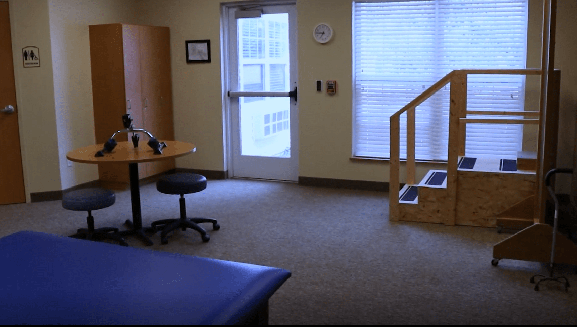 A physical therapy room equipped with a therapy table, exercise area, and basic rehabilitation equipment.