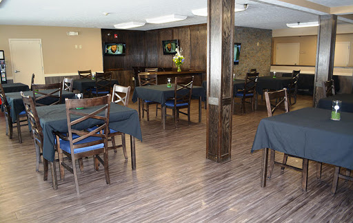 A spacious and modern restaurant interior featuring wooden flooring, dark tables, and a welcoming bar area.