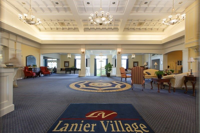 A spacious lobby with elegant chandeliers, comfortable seating areas, and a carpet bearing the name Lanier Village.