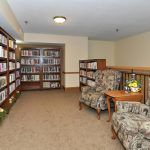 A cozy library with bookshelves, armchairs, and a carpeted reading area.