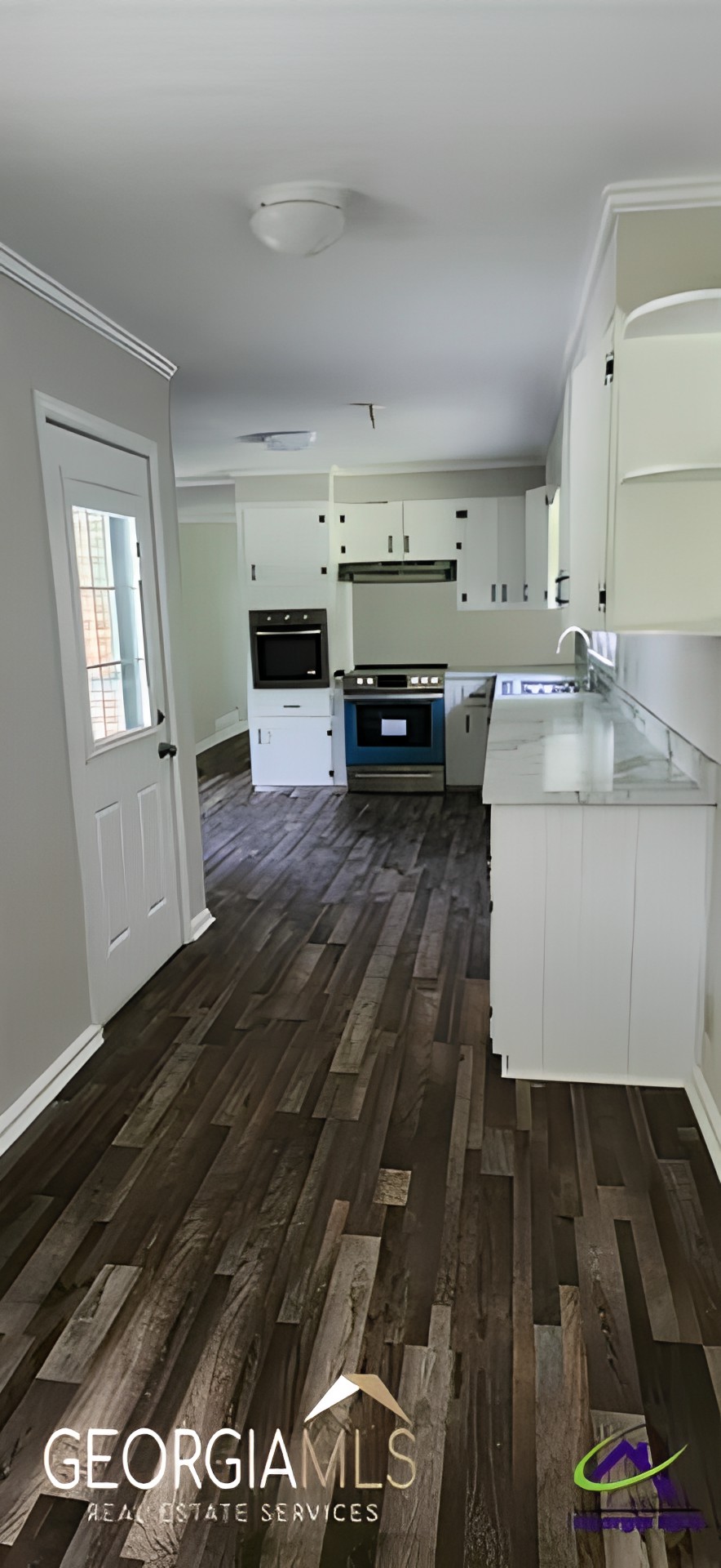 A modern kitchen with white cabinets and dark wood flooring.