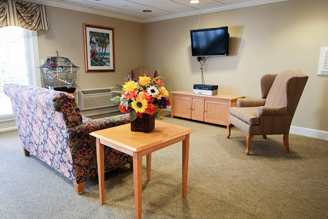 A cozy living room with comfortable seating, a bouquet of flowers on the table, and a television mounted on the wall.