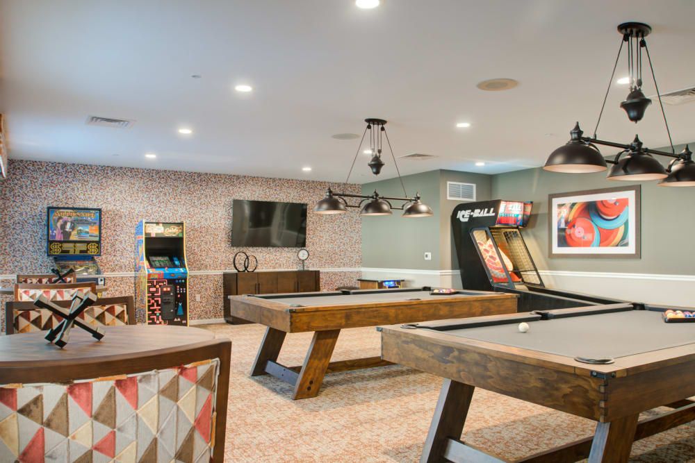 A modern game room featuring pool tables, an arcade machine, and a wall-mounted TV.