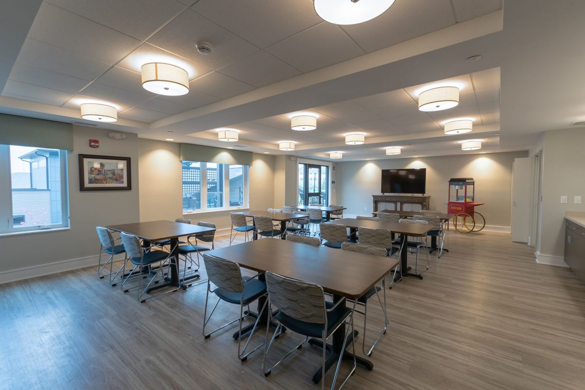 A modern, spacious dining area with multiple tables and chairs, illuminated by ceiling lights.
