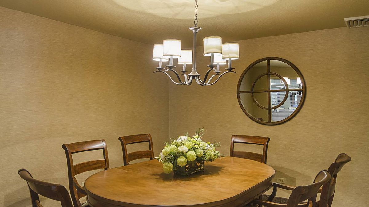 A cozy dining room with a wooden table, surrounded by chairs, featuring a chandelier and decorative mirror.