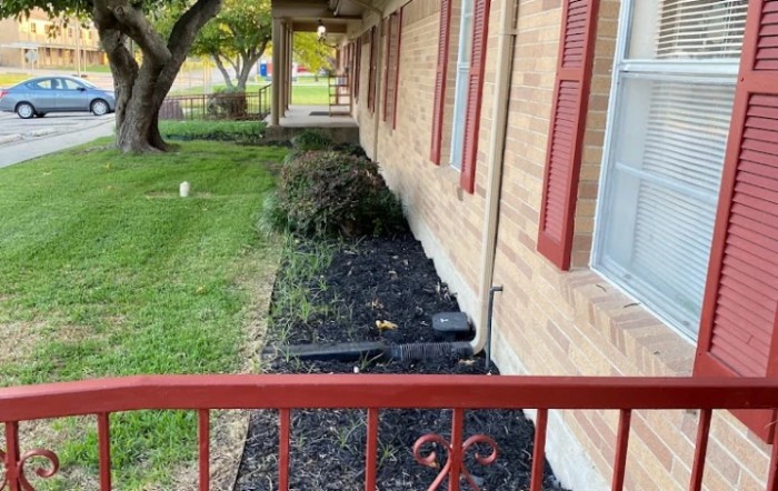 A landscaped garden bed along the side of a house with mulch and bushes.