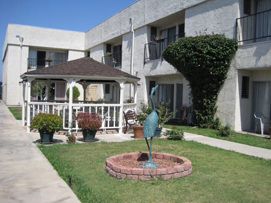 A well-maintained garden area with a gazebo and fountain in front of an apartment building.