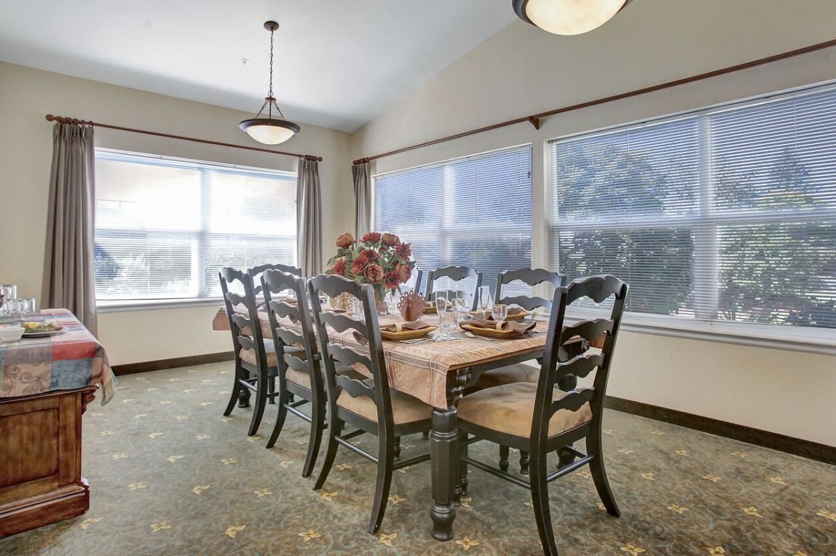 A well-lit dining room with a wooden table and matching chairs, featuring large windows and elegant decor.