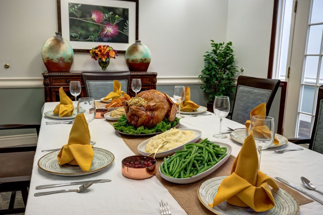 A beautifully set Thanksgiving dinner table with a roasted turkey, green beans, mashed potatoes, and elegant place settings.