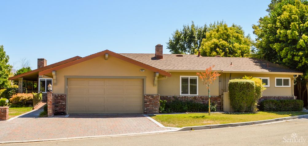 A single-story suburban house with a driveway and garage, surrounded by trees.