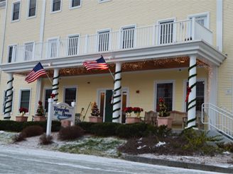 A building with flags and winter decorations on the porch, surrounded by light snow.