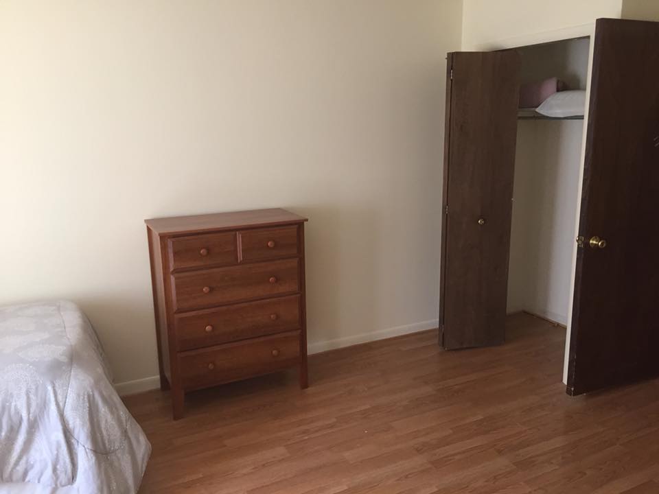 A minimalist bedroom with a wooden dresser and an open closet.