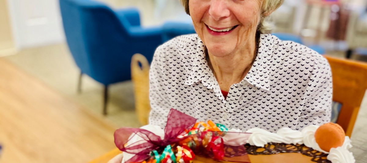 An elderly woman smiling while holding a festively wrapped gift indoors.