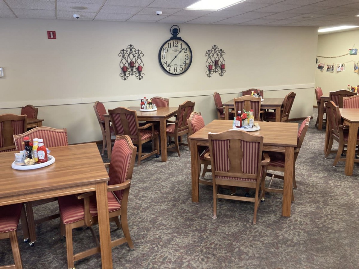 A dining area with wooden tables and chairs, decorated with a large wall clock and ornaments.
