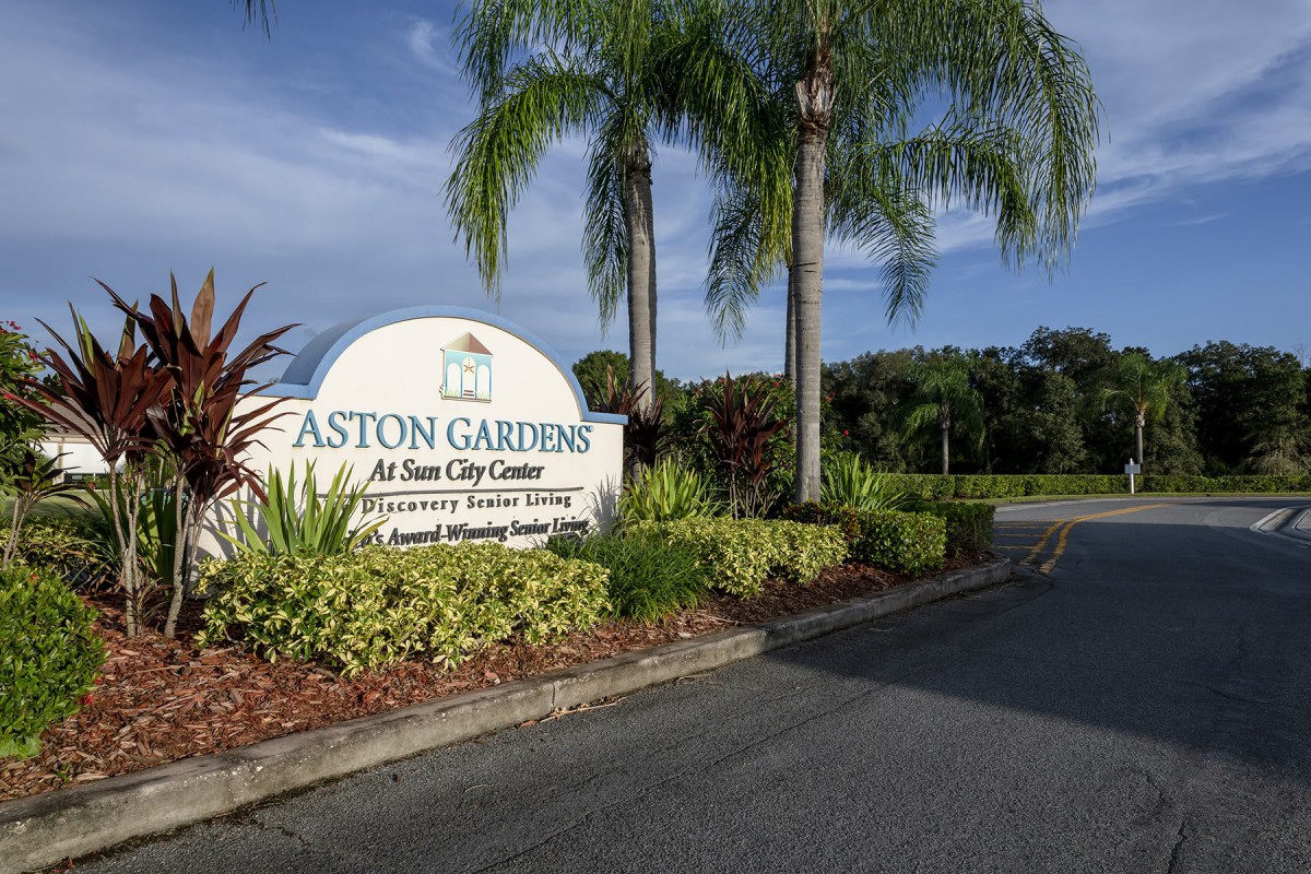 Signage of Aston Gardens, a senior living community, surrounded by palm trees and landscaping.