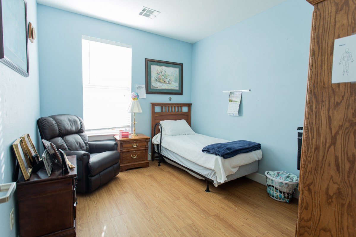 A neatly arranged bedroom with blue walls, featuring a single bed, armchair, nightstand, and wall art.