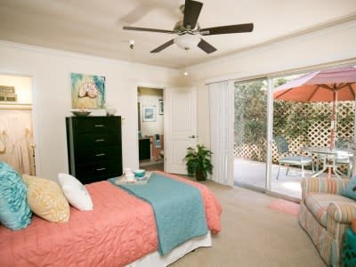 A cozy bedroom featuring a bed with colorful linens, a ceiling fan, and ample natural light from sliding doors.