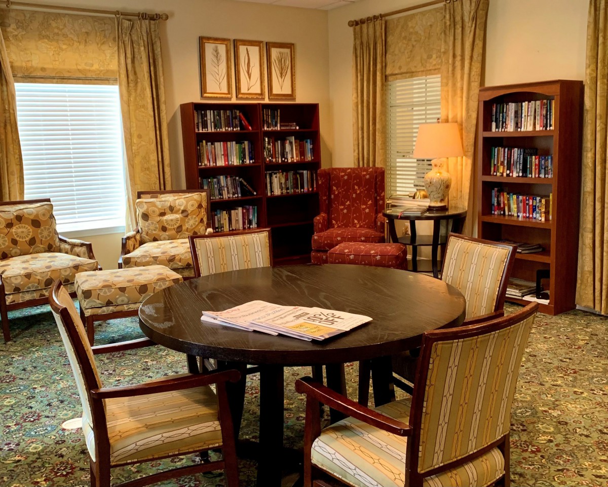 A cozy library with bookshelves, comfortable chairs, and a round table.