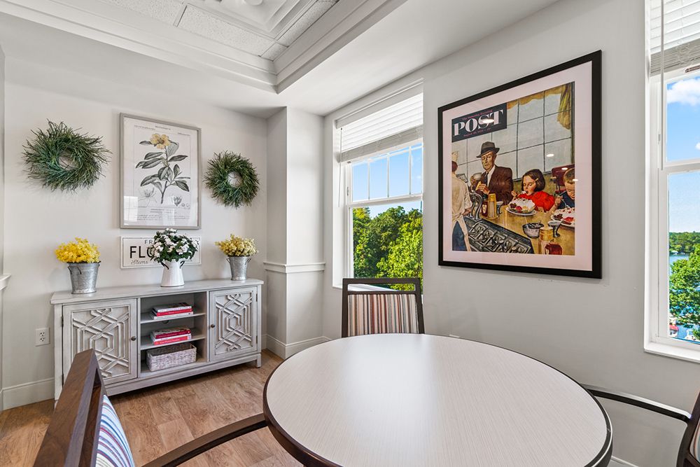 A cozy dining room with a round table, contemporary artwork on the wall, and a window offering a view of lush greenery.