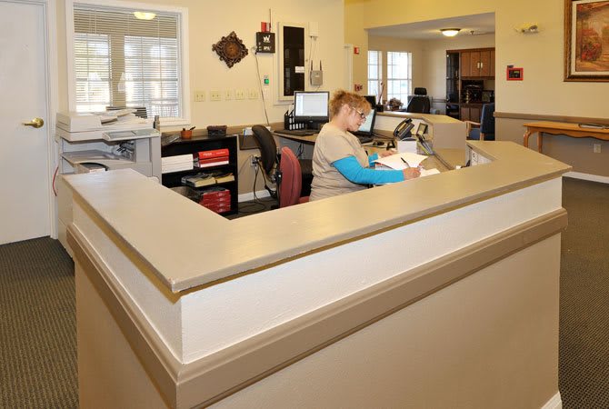 An office reception area with a seated employee working at a desk.