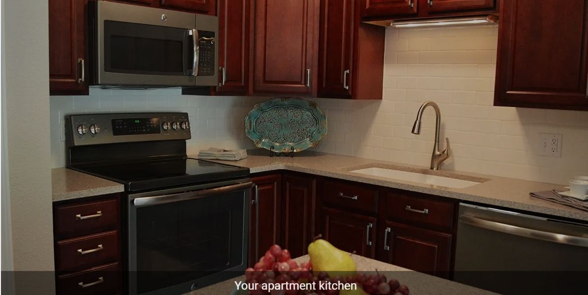 A modern apartment kitchen with wooden cabinets and stainless steel appliances.