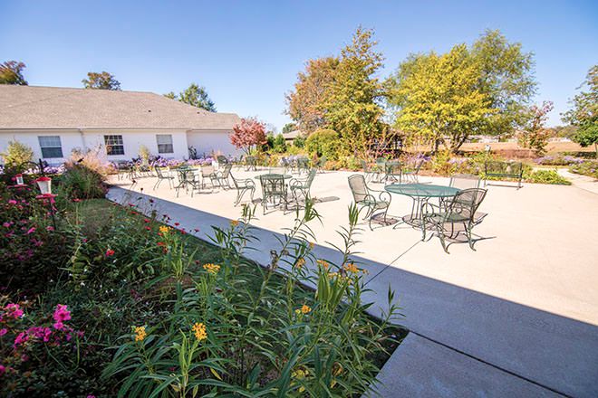 Outdoor patio area with tables and chairs surrounded by greenery.