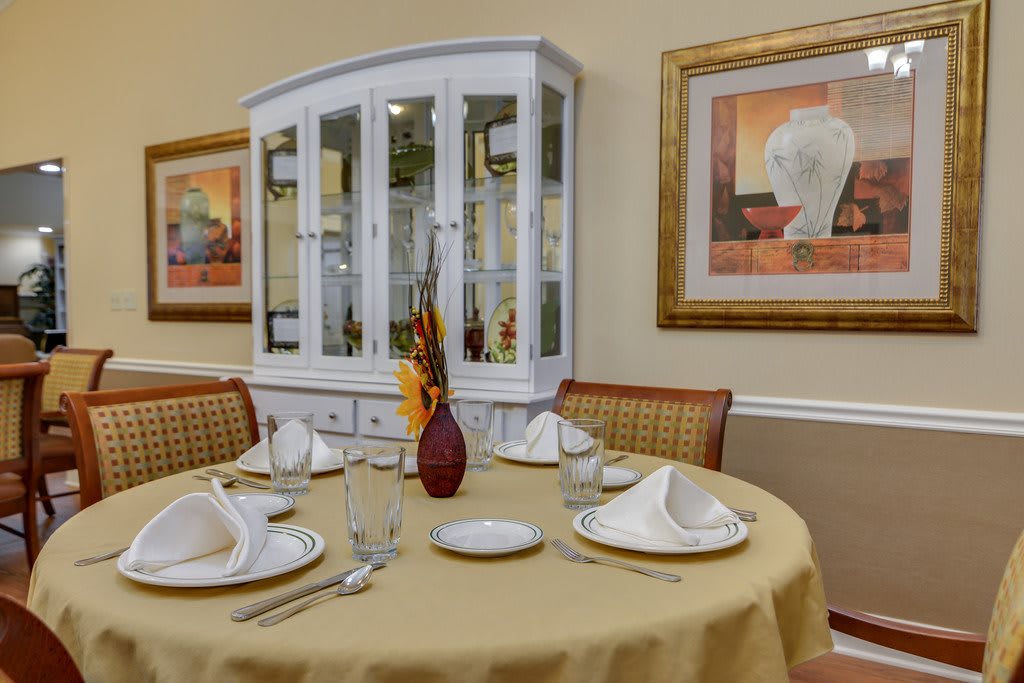 An elegantly set dining table with a china cabinet and artwork in the background.