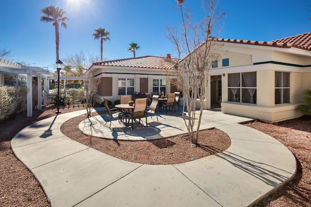 A sunny outdoor patio area with chairs and tables, surrounded by palm trees and a residential building.