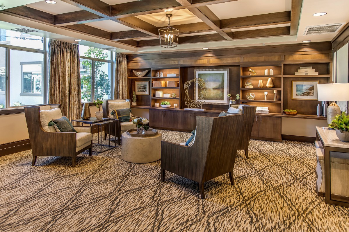 A cozy and elegant living room featuring comfortable seating, wooden bookshelves, and a large window with natural light.