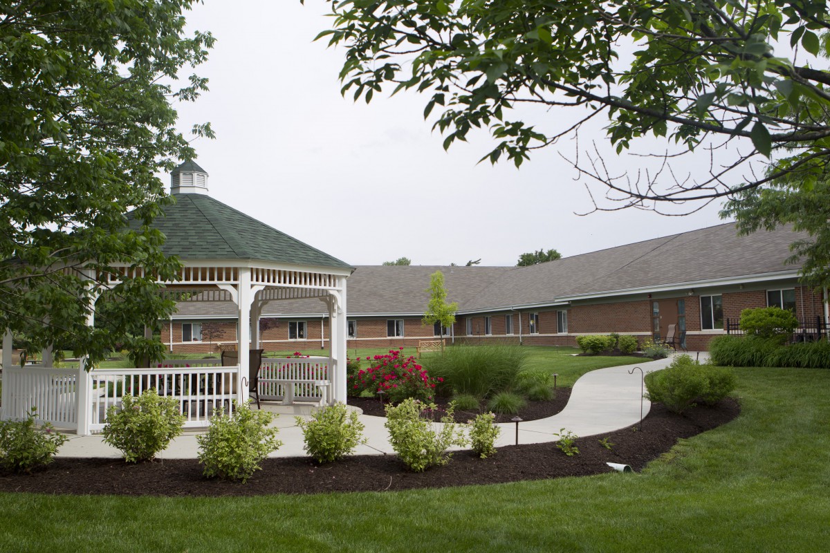 A scenic view of a gazebo and pathway surrounded by lush gardens and a building in the background.