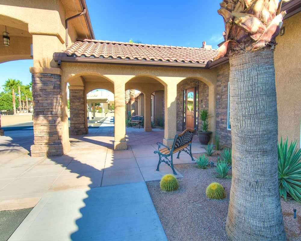 A sunny view of a house with a covered porch and desert landscaping.