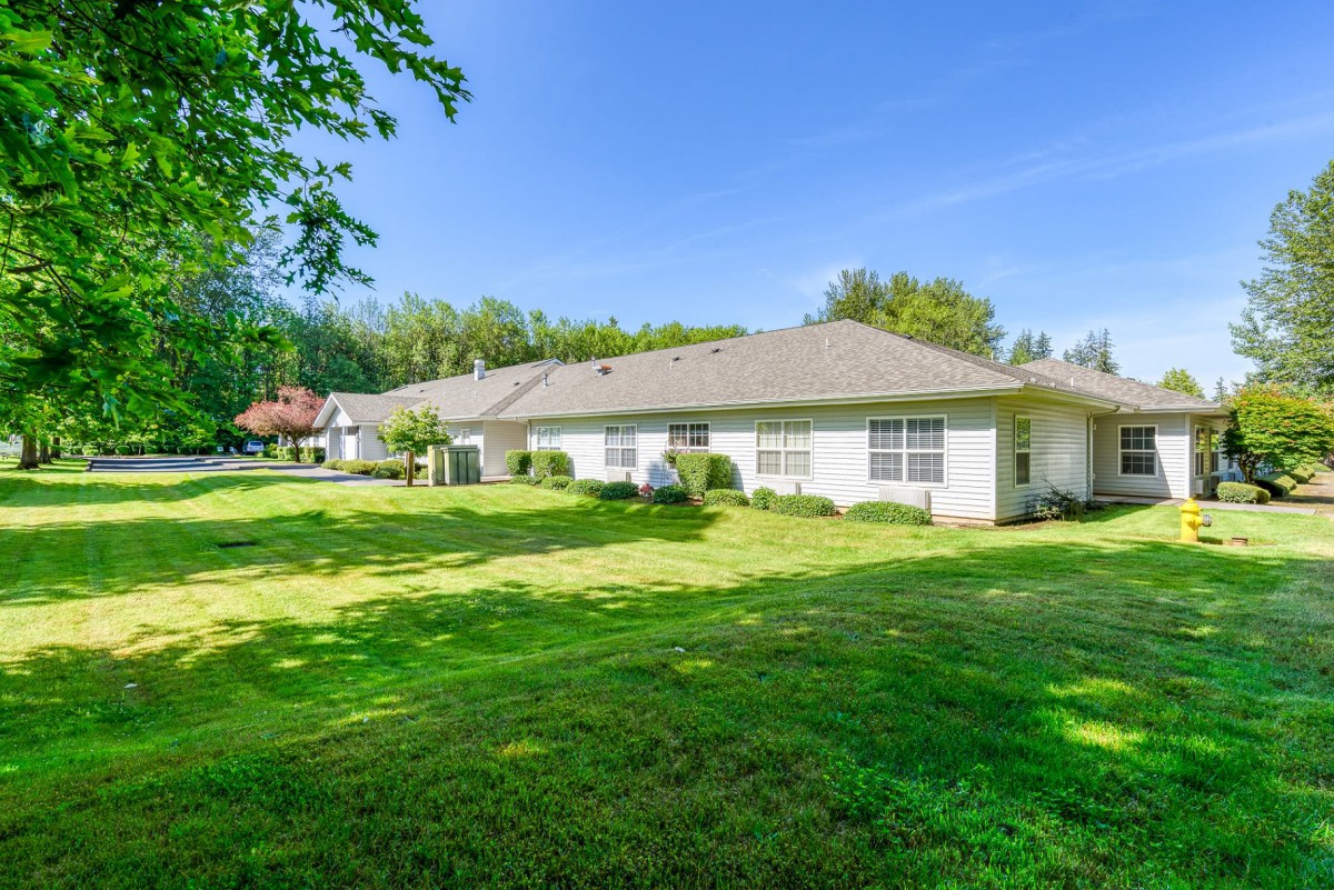 A single-story residential house with a well-maintained lawn and surrounding trees under a clear blue sky.