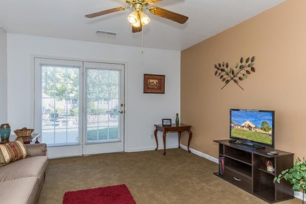 A cozy living room featuring a ceiling fan, television, decorative wall art, and glass doors leading to the outside.