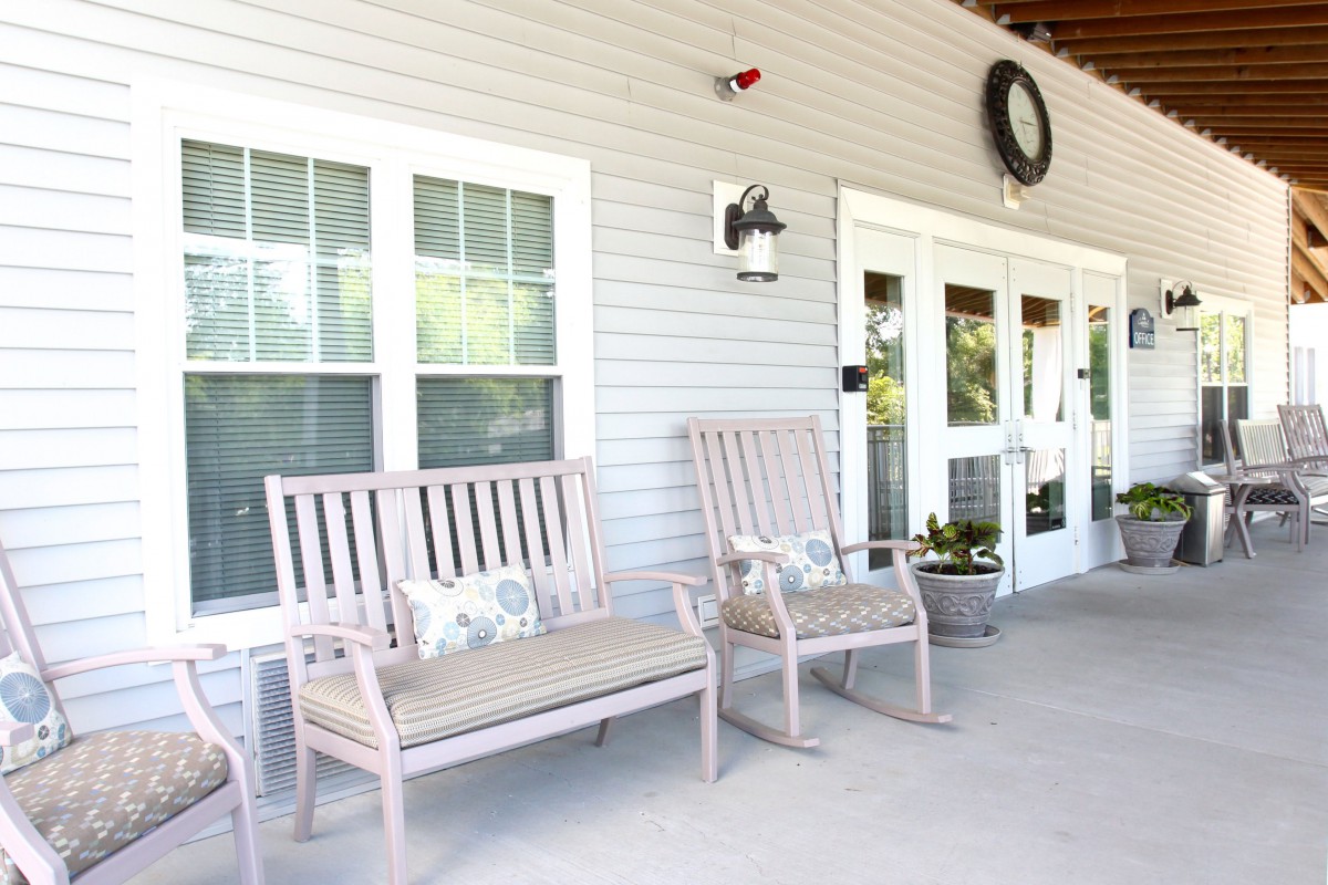 A cozy porch with benches and rocking chairs, complemented by a decorative wreath and wall-mounted light.