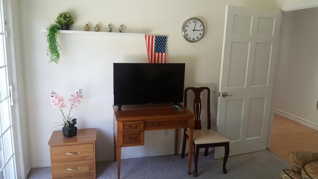 A living room setup featuring a television on a wooden desk, an American flag, and a wall clock.