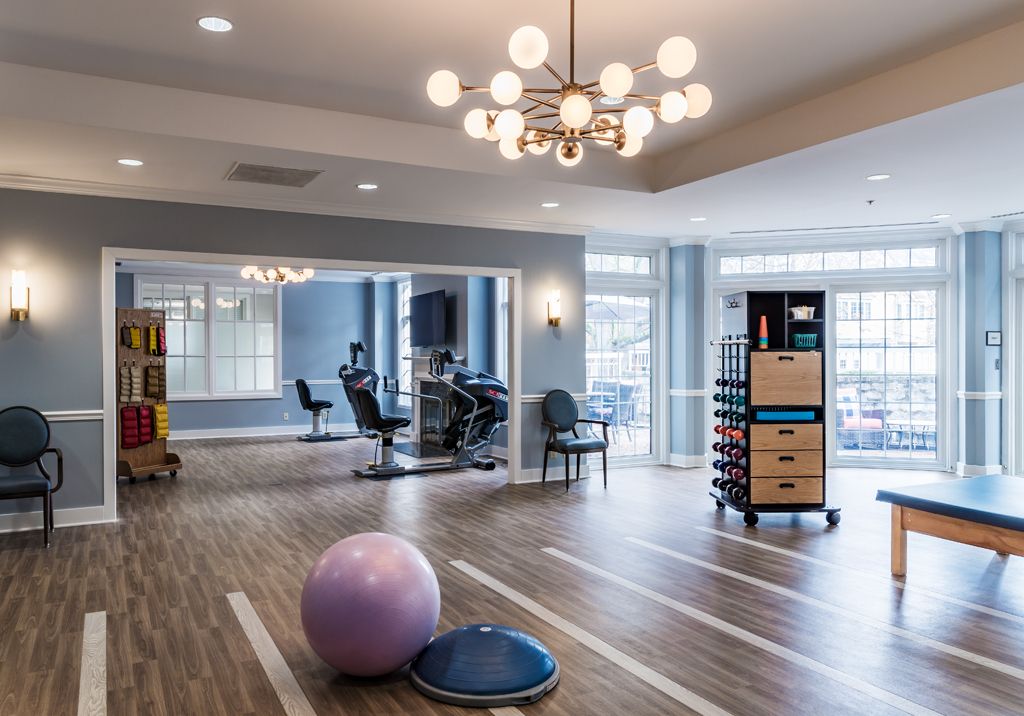 A modern exercise room equipped with fitness equipment, therapy balls, and large mirrors.