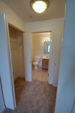 A view of a bathroom with an adjacent closet, featuring a sink, toilet, and mirror.