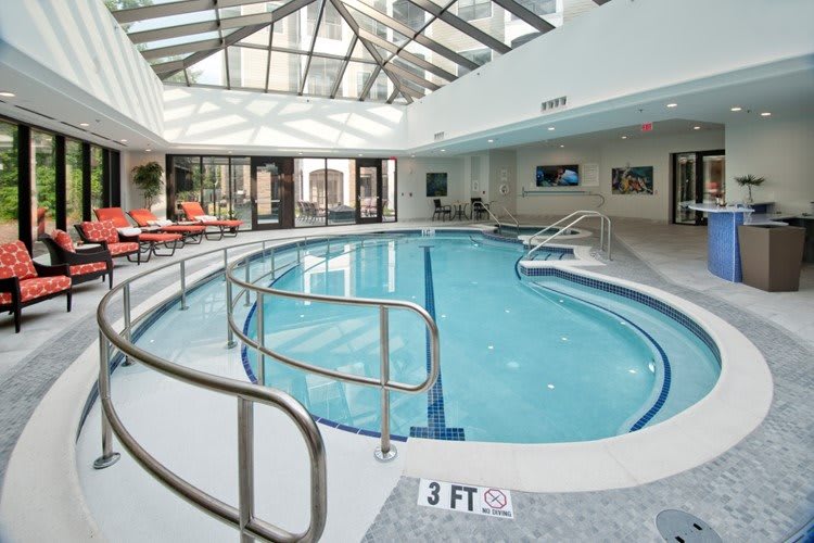 A serene indoor swimming pool with a glass ceiling and relaxation chairs.