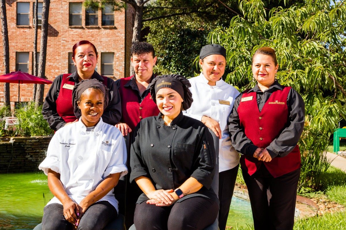 A group of chefs and staff posing outdoors in their uniforms.
