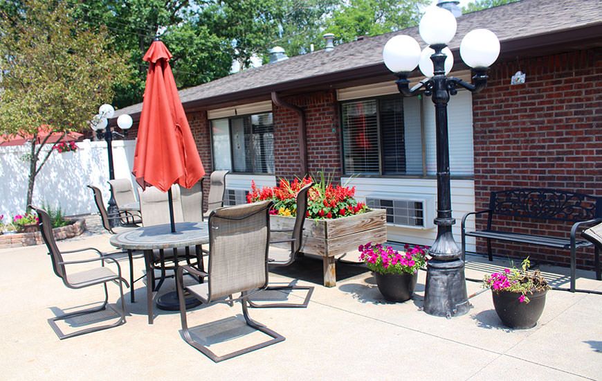 A cozy outdoor patio area with a table, chairs, and vibrant flowers.